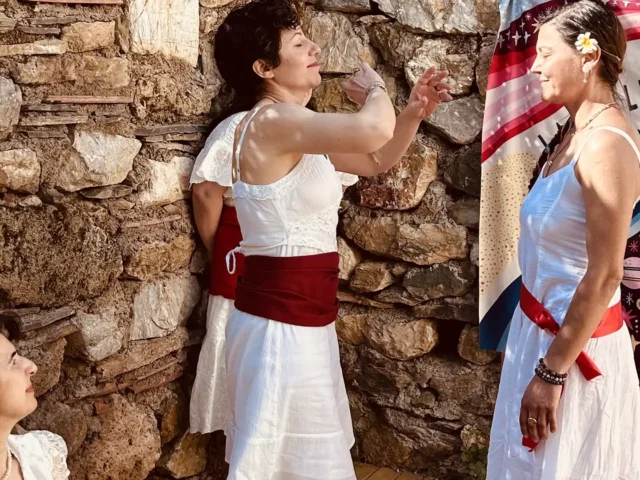 Beyaz elbiseli üç kadın Munay Ki töreninde, kozmik desenli pankart önünde