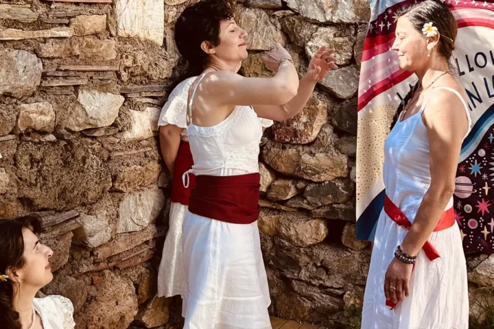 Beyaz elbiseli üç kadın Munay Ki töreninde, kozmik desenli pankart önünde