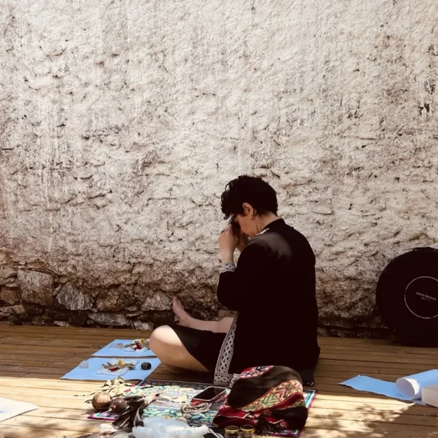 Özbilen Duygu taş duvar önünde şamanik objeler ve kristallerle hazırlık meditasyonunda